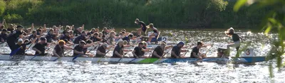 Auf einem Fluss sind drei Drachenboote zu sehen, die gegeneinander antreten