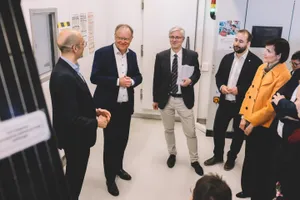 Eine Gruppe mehrerer Personen steht in einem Maschinenraum und hört einem Mann zu
