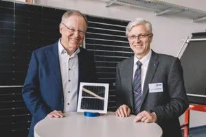 Zwei Männer im Anzug stehen an einem Tisch, auf dem ein PV-Modul steht.