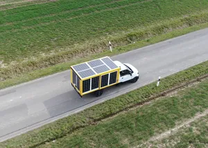 Luftaufnahme einer Straße, auf der ein mit PV-Modulen verkleideter Kleintransporter fährt