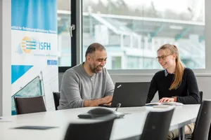 Zwei Mitarbeitende sitzen gemeinsam am Tisch und gucken auf einen Laptop
