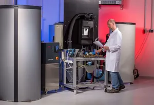 A technician in a white lab coat works at a test station for thermal energy converters, positioned between two large thermal storage units.