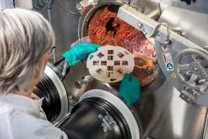 Eine Mitarbeiterin baut einen Probenhalter in eine Aufdampfanlage ein.