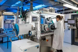 Eine Laborkraft steht an einer Maschine zur Perowskit-Dünnschichtherstellung.