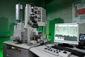 A monitor shows an image of the scanning electron microscope standing next to it.