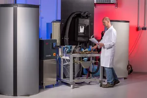 A technician in a white lab coat works at a test station for thermal energy converters between two large heat storage tanks.
