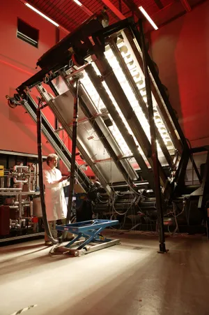 Technician testing a solar thermal collector under a high-temperature solar simulator in a red-lit laboratory.
